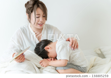 Mother reading a picture book to her child in bed (putting to sleep, nap, reading aloud) Mother reading a picture book to her child in bed (putting to sleep, nap, reading aloud) 138805259