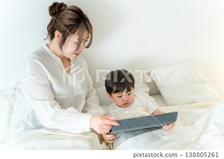 A mother reading a picture book to her child on a tablet while they are in bed (for bedtime, nap time, and story time). 138805261