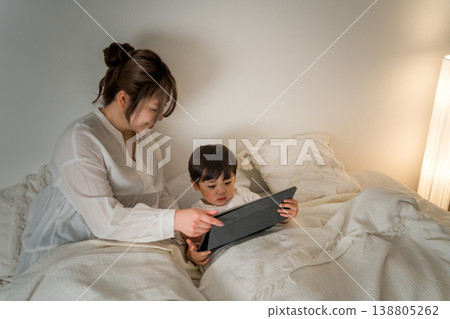A mother reading a picture book to her child on a tablet while they are in bed (for bedtime, nap time, and story time). 138805262