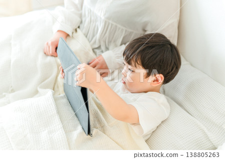 A mother reading a picture book to her child on a tablet while they are in bed (for bedtime, nap time, and story time). A mother reading a picture book to her child on a tablet while they are in bed (for bedtime, nap time, and story time). 138805263