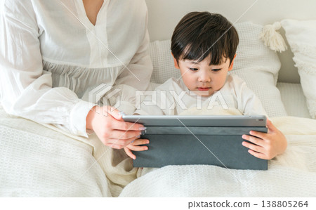 A mother reading a picture book to her child on a tablet while they are in bed (for bedtime, nap time, and story time). 138805264