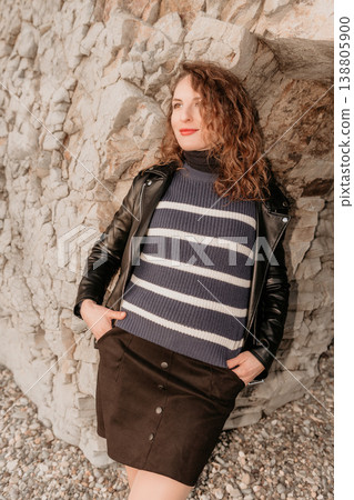 Woman leather jacket rock wall leaning against a textured stone cliff outdoors while wearing casual stylish autumn layers Woman leather jacket rock wall leaning against a textured stone cliff outdoors while wearing casual stylish autumn layers 138805900
