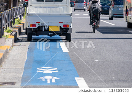 A parent and child on bicycles taking the road to avoid parked cars and the resulting traffic risks. A parent and child on bicycles taking the road to avoid parked cars and the resulting traffic risks. 138805963