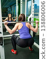 Young woman squatting with barbell in front of mirror at gym, fitness training concept 138806006