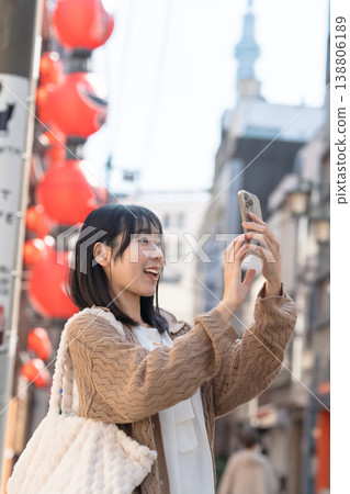 A smiling woman takes photos with her smartphone while walking through a downtown area with a view of the Tokyo Skytree. A smiling woman takes photos with her smartphone while walking through a downtown area with a view of the Tokyo Skytree. 138806189