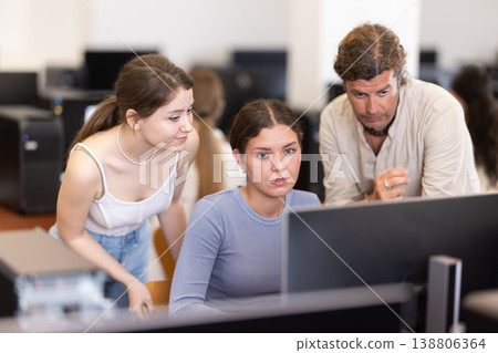 During computer lesson, two companions help girl student complete difficult task During computer lesson, two companions help girl student complete difficult task 138806364
