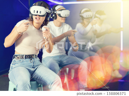 In darkened hall of gaming club, girl in VR helmet takes part in group game In darkened hall of gaming club, girl in VR helmet takes part in group game 138806371