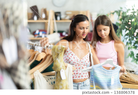Positive mother and teenage daughter choosing something for summer in clothing store Positive mother and teenage daughter choosing something for summer in clothing store 138806378