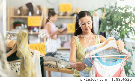 Middle-aged woman choosing something for summer in clothing store Middle-aged woman choosing something for summer in clothing store 138806529