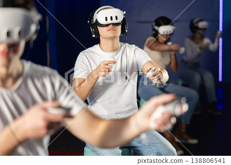 In darkened hall of gaming club, guy in VR helmet takes part in group game In darkened hall of gaming club, guy in VR helmet takes part in group game 138806541