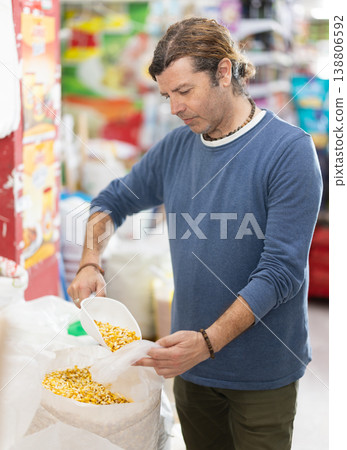 Man in store takes maize cereal out of sack, pours dose of cereal into bag 138806592