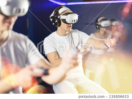 In darkened hall of gaming club, guy in VR helmet takes part in group game 138806633
