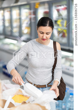 Woman in store takes maize grits cereal out of sack, pours dose of cereal into bag Woman in store takes maize grits cereal out of sack, pours dose of cereal into bag 138806716