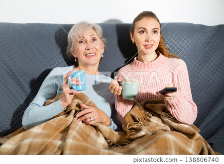 Happy elderly woman with adult daughter drinking tea and watching movie Happy elderly woman with adult daughter drinking tea and watching movie 138806740