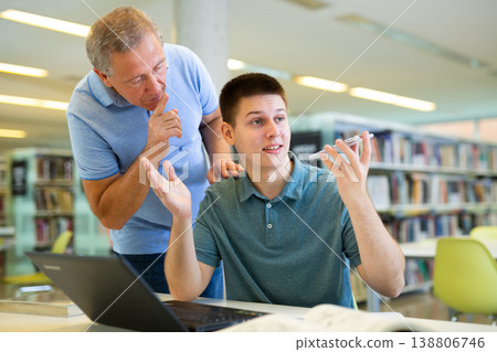 Elderly librarian asks young man who is talking loudly on mobile phone to keep quiet 138806746