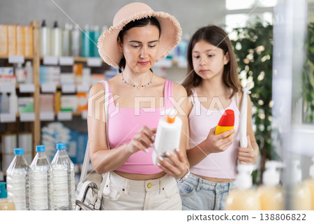 Mom and daughter choosing sunscreen in chemist's shop Mom and daughter choosing sunscreen in chemist's shop 138806822