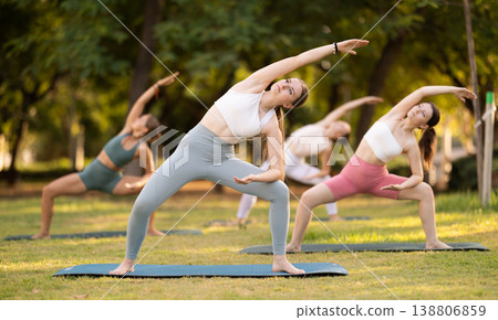 Slim women practicing yoga - virabhadrasana pose in summer park Slim women practicing yoga - virabhadrasana pose in summer park 138806859