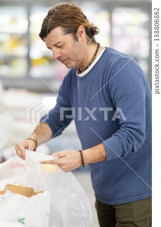 Man in store takes maize grits cereal out of sack, pours dose of cereal into bag Man in store takes maize grits cereal out of sack, pours dose of cereal into bag 138806862