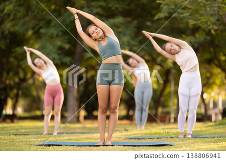 Fitness, sport and healthy lifestyle concept: girls doing yoga yoga pose - vrikshasana pose on mat in park Fitness, sport and healthy lifestyle concept: girls doing yoga yoga pose - vrikshasana pose on mat in park 138806941