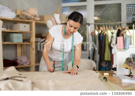 Woman seamstress cuts fabric on cutting table Woman seamstress cuts fabric on cutting table 138806990