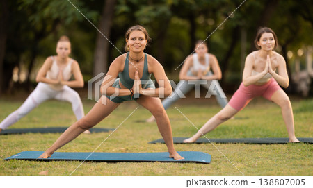 Yoga lesson visitors girls perform skandasana in park 138807005