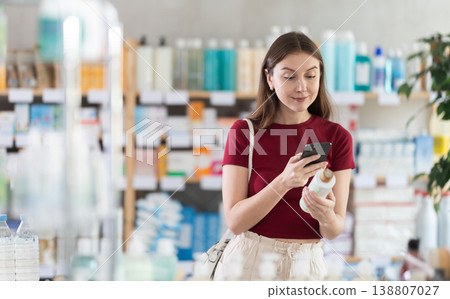 Woman in pharmacy scans QR code on antidandruff shampoo 138807027