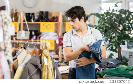 Young man in store chooses jeans or jacket. Young man in store chooses jeans or jacket. 138807043