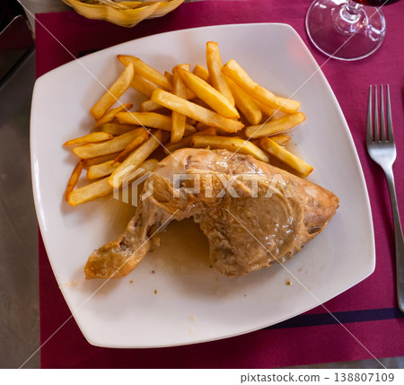 Baked chicken leg served on plate with side dish of fried potatoes 138807109