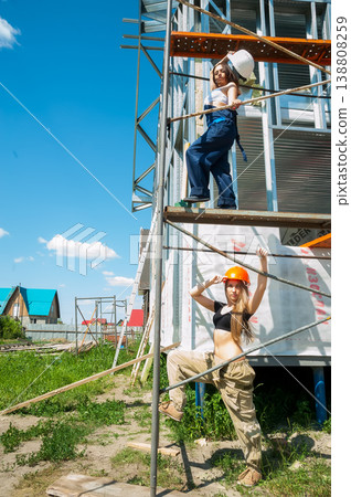 Two women in hard hats standing on scaffolding at a residential construction site, safety and teamwork concept Two women in hard hats standing on scaffolding at a residential construction site, safety and teamwork concept 138808259