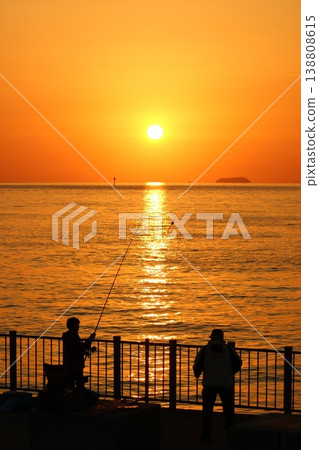 A person fishing towards the sunset over the sea. A person fishing towards the sunset over the sea. 138808615
