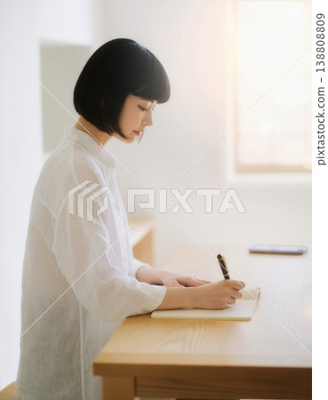 一位女士側臉凝視著自己，神情專注地在書桌前的筆記本上書寫。 138808809