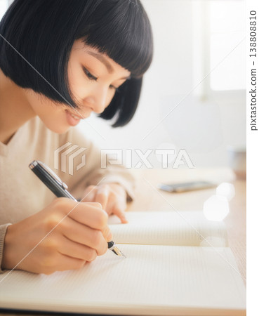 一位女士用鋼筆在筆記本上寫字，她的手和側臉清晰可見。 138808810