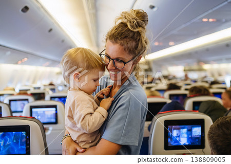 Mom calming upset child during family flight while traveling on airplane. 138809005