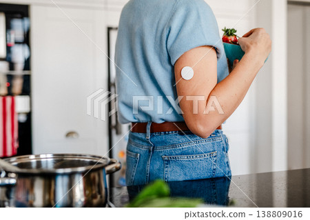 Mature woman with CGM glucose sensor preparing healthy meal at home kitchen. 138809016