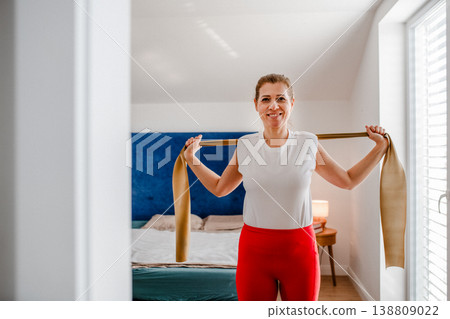 Smiling middle aged woman exercising with resistance band at home. Smiling middle aged woman exercising with resistance band at home. 138809022