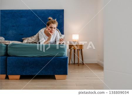 Middle aged woman using smartphone while lying in bed at home. Middle aged woman using smartphone while lying in bed at home. 138809034