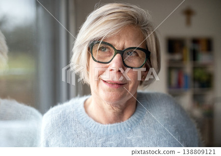 Smiling elderly woman looking through window at home. 138809121