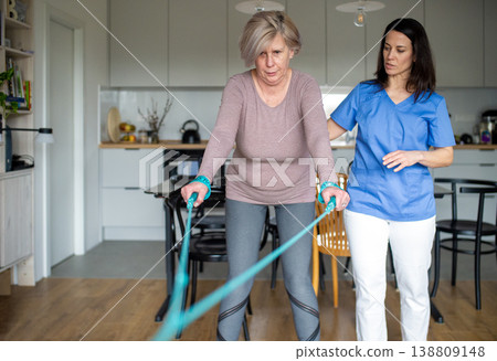 Physiotherapist guiding senior woman during resistance band exercise. 138809148