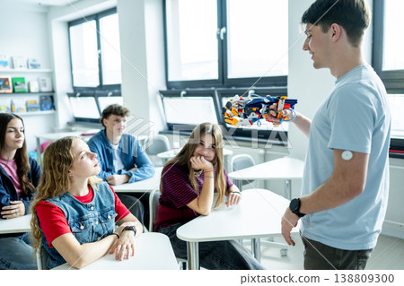Teen boy presenting robotic project in front of classroom. Teen boy presenting robotic project in front of classroom. 138809300