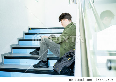 Depressed male student sitting on stairs and looking at phone. Depressed male student sitting on stairs and looking at phone. 138809306