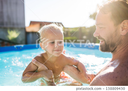 Little boy splashing and playing in pool with dad. 138809430
