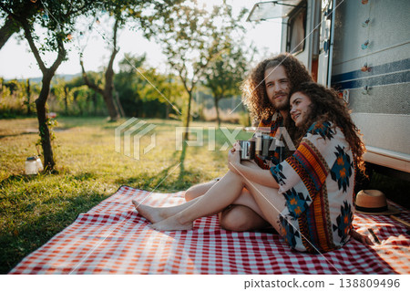 Beautiful couple sitting in front of caravan under blanket, enjoying peaceful moment, drinking coffee of herbal tea. 138809496