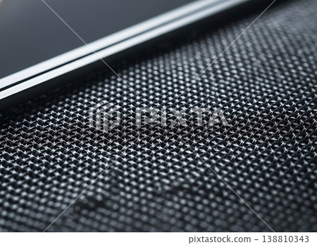 Close-up view of textured black mesh fabric with geometric patterns and shiny surface, showcasing intricate details and modern design elements in a contemporary setting 138810343