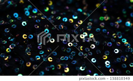 Close-up view of shimmering black fabric adorned with multicolored sequins reflecting light, creating a vibrant and textured surface ideal for fashion or decoration Close-up view of shimmering black fabric adorned with multicolored sequins reflecting light, creating a vibrant and textured surface ideal for fashion or decoration 138810349