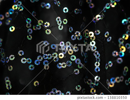 Close-up of colorful sequins on black fabric, showcasing a shimmering texture with various sizes and reflections, ideal for fashion or textile design applications 138810350