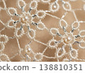 Intricate lace fabric with floral patterns featuring pearls and silver threads, showcasing detailed craftsmanship and texture against a soft beige background 138810351