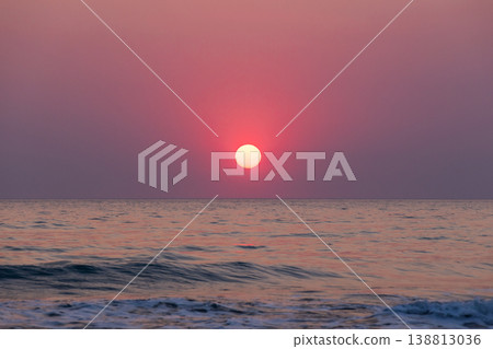 A tranquil sea view at dusk features a red pink sun sinking toward the horizon A tranquil sea view at dusk features a red pink sun sinking toward the horizon 138813036
