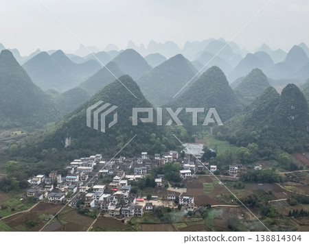 Misty hills rise gently behind a quiet village of Yangshuo, Guangxi Province, China Misty hills rise gently behind a quiet village of Yangshuo, Guangxi Province, China 138814304