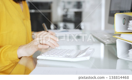 Accountant in yellow blouse working on financial budget, calculating taxes and expenses, managing paperwork in office. Audit and taxes in business Accountant in yellow blouse working on financial budget, calculating taxes and expenses, managing paperwork in office. Audit and taxes in business 138814468