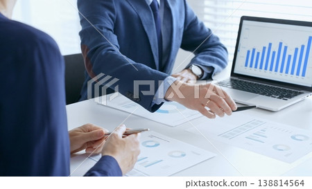 Business team analyzing financial data on a laptop and printed documents, pointing at charts and graphs during a meeting. Business people and finance concept 138814564